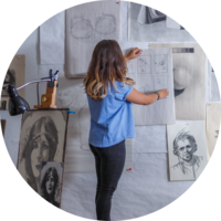 A female student hangs sketches on the wall.